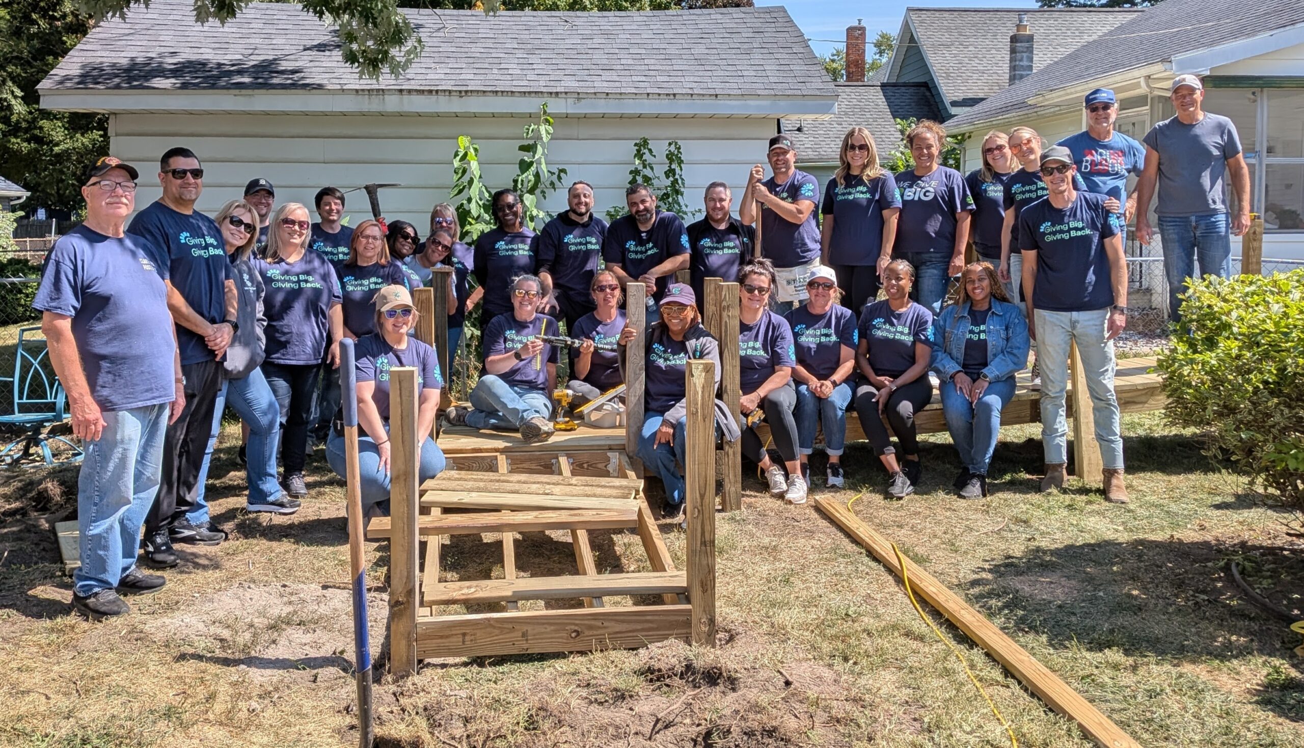 Large group of volunteers pose around a newly built garden bed in a residential yard, supporting food access and community gardening efforts.